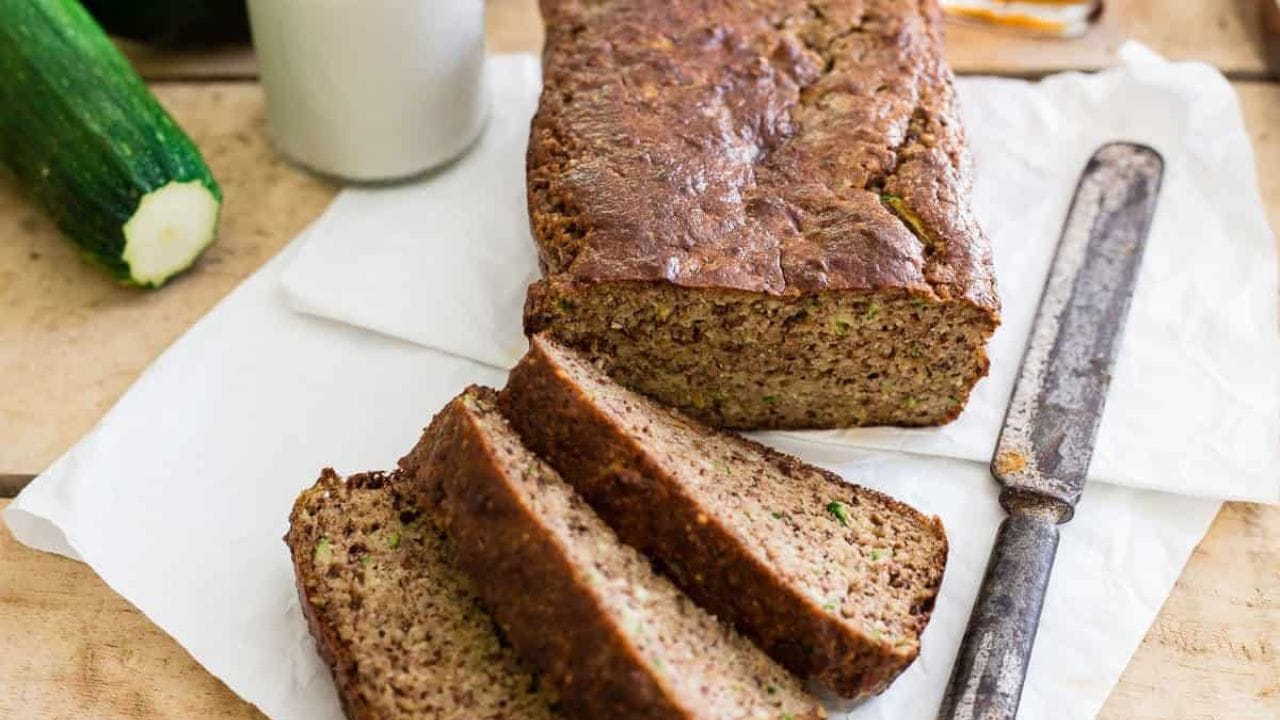 Paleo almond zucchini bread cut into slices with jug of milk, knife and zucchini to the side.
