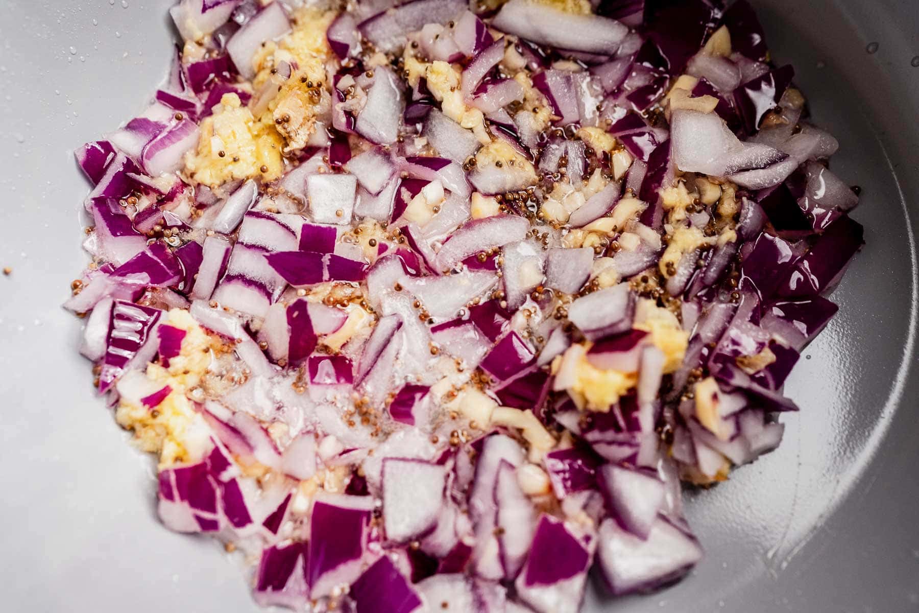 Chopped red onions and minced garlic sautéing in oil in a pan, perfect as a base for adding mango chutney.