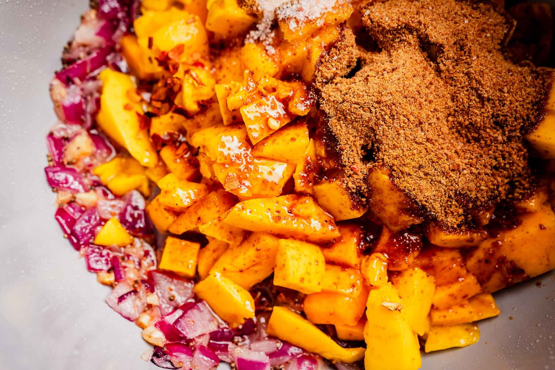 Chopped mango, red onion, spices, and seasonings are mixed together in a bowl, creating a flavorful base for a homemade mango chutney or salsa.