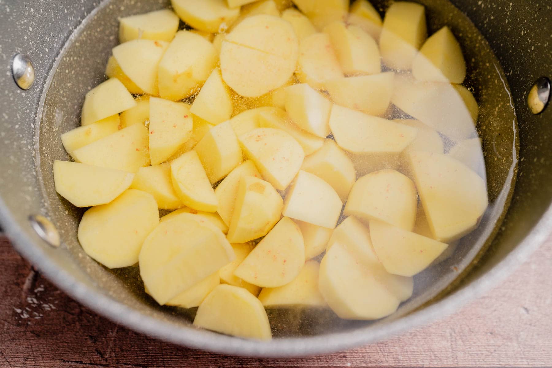 Chopped potatoes submerged in water inside a large metal pot, ready to be transformed into cheesy mashed potatoes.
