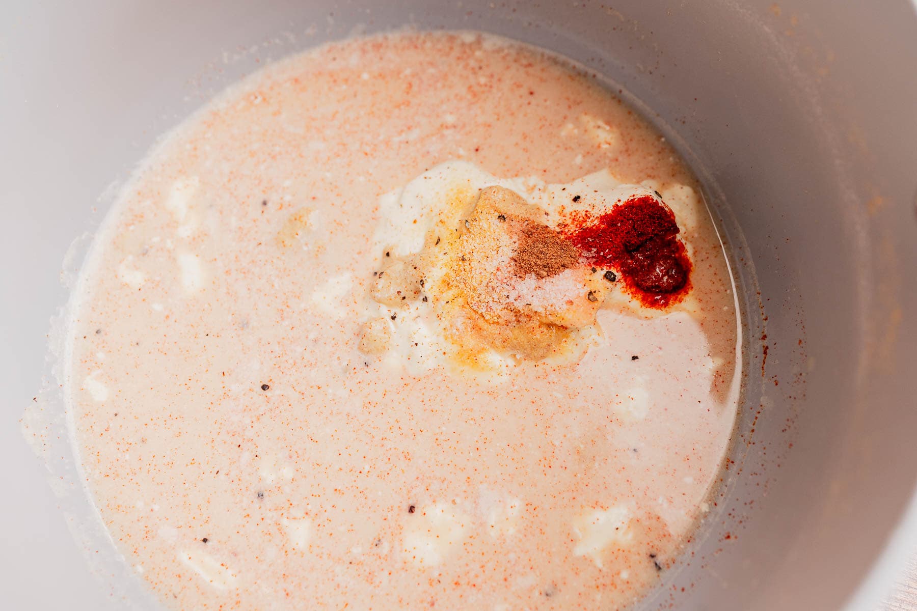 A bowl containing a mixture of cream, spices, and seasonings, with visible red and yellow spices on the surface—perfect as a sauce base for gluten free mac and cheese.