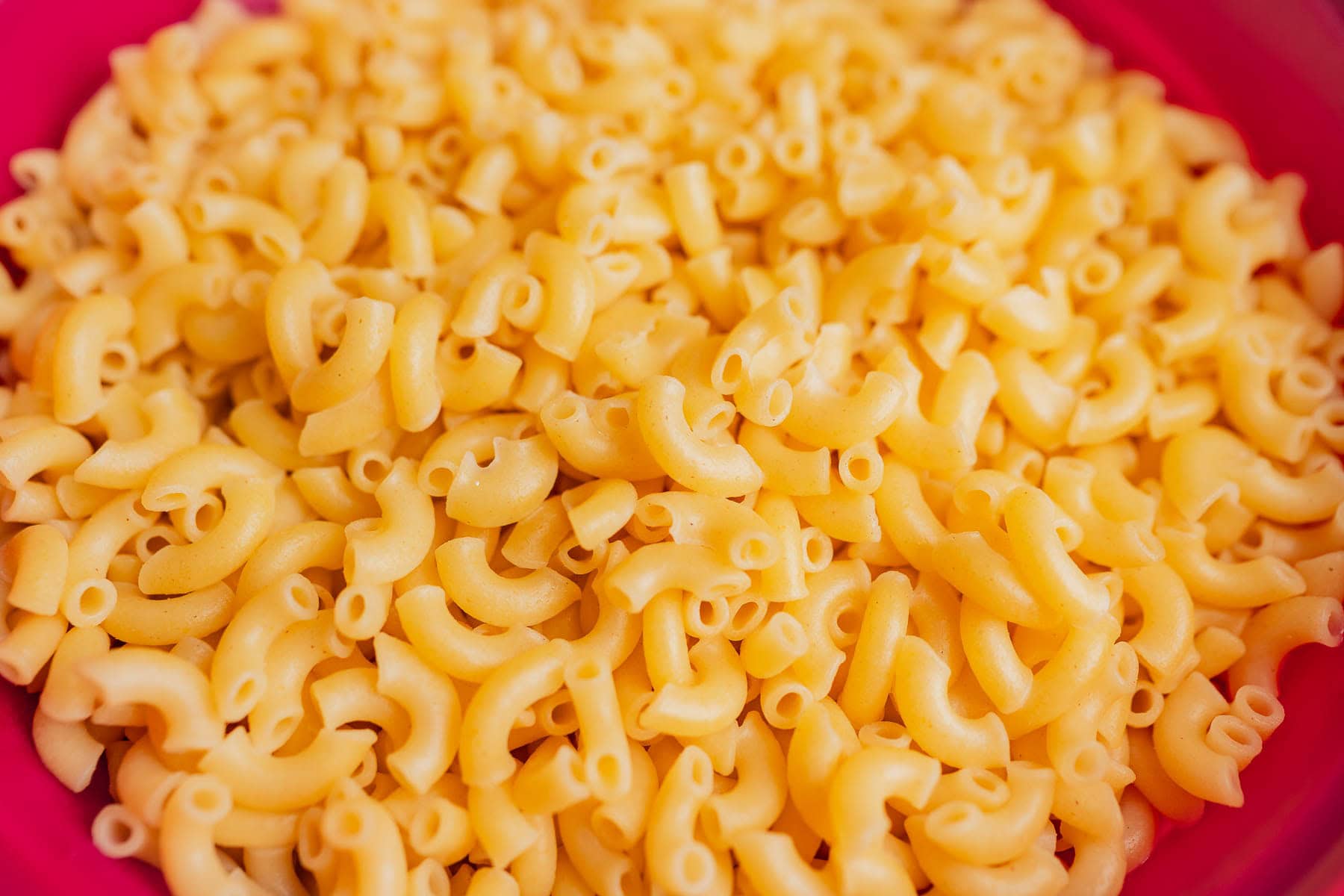 Close-up view of cooked gluten free mac and cheese elbow macaroni pasta on a pink plate.