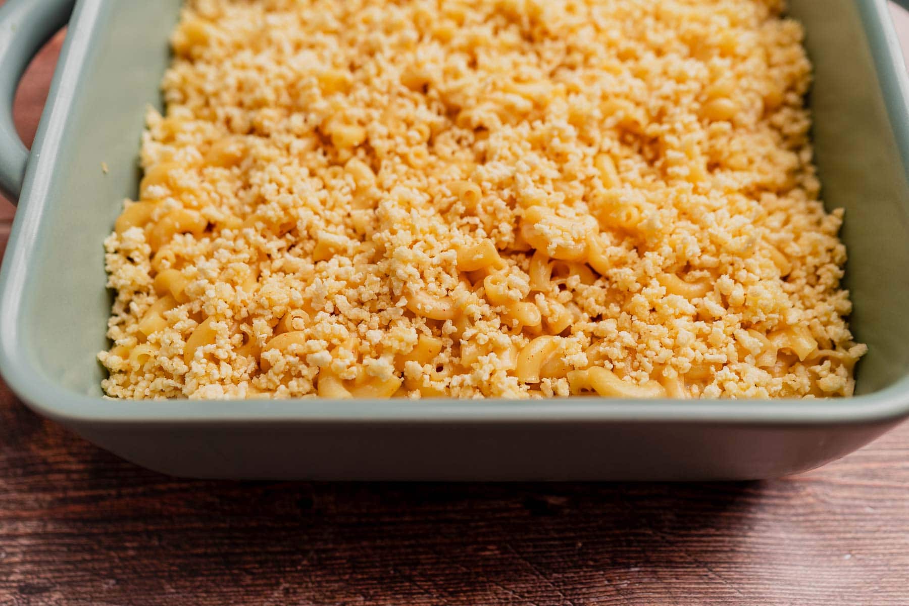 A baking dish filled with gluten free mac and cheese, topped with a layer of crunchy breadcrumbs, sits on a wooden surface.