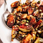 A plate of roasted Brussels sprouts garnished with chopped nuts, served with a spoon for easy sharing.