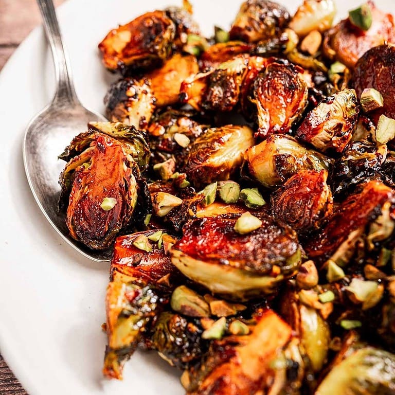 A plate of roasted Brussels sprouts garnished with chopped nuts, served with a spoon for easy sharing.