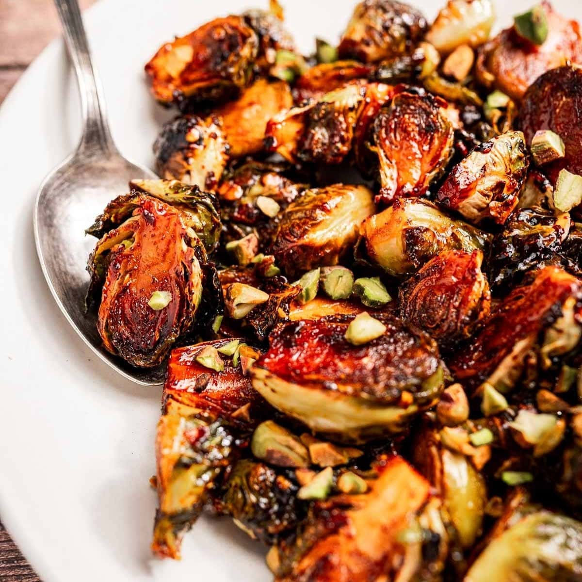 A plate of roasted Brussels sprouts garnished with chopped nuts, served with a spoon for easy sharing.