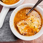 Bowl of vegetarian French onion soup topped with a slice of melted cheese and bread, with a spoon resting inside, on a striped napkin.