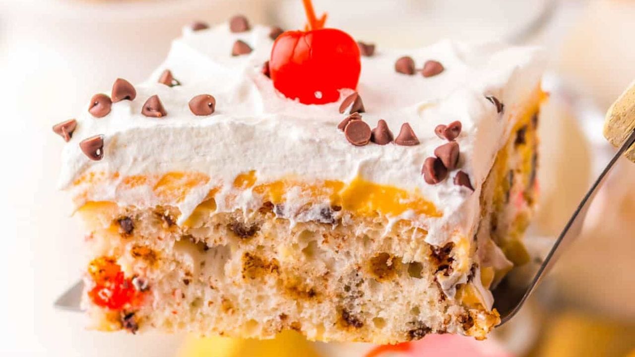 A slice of cake with whipped topping, cherries and chocolate chip.