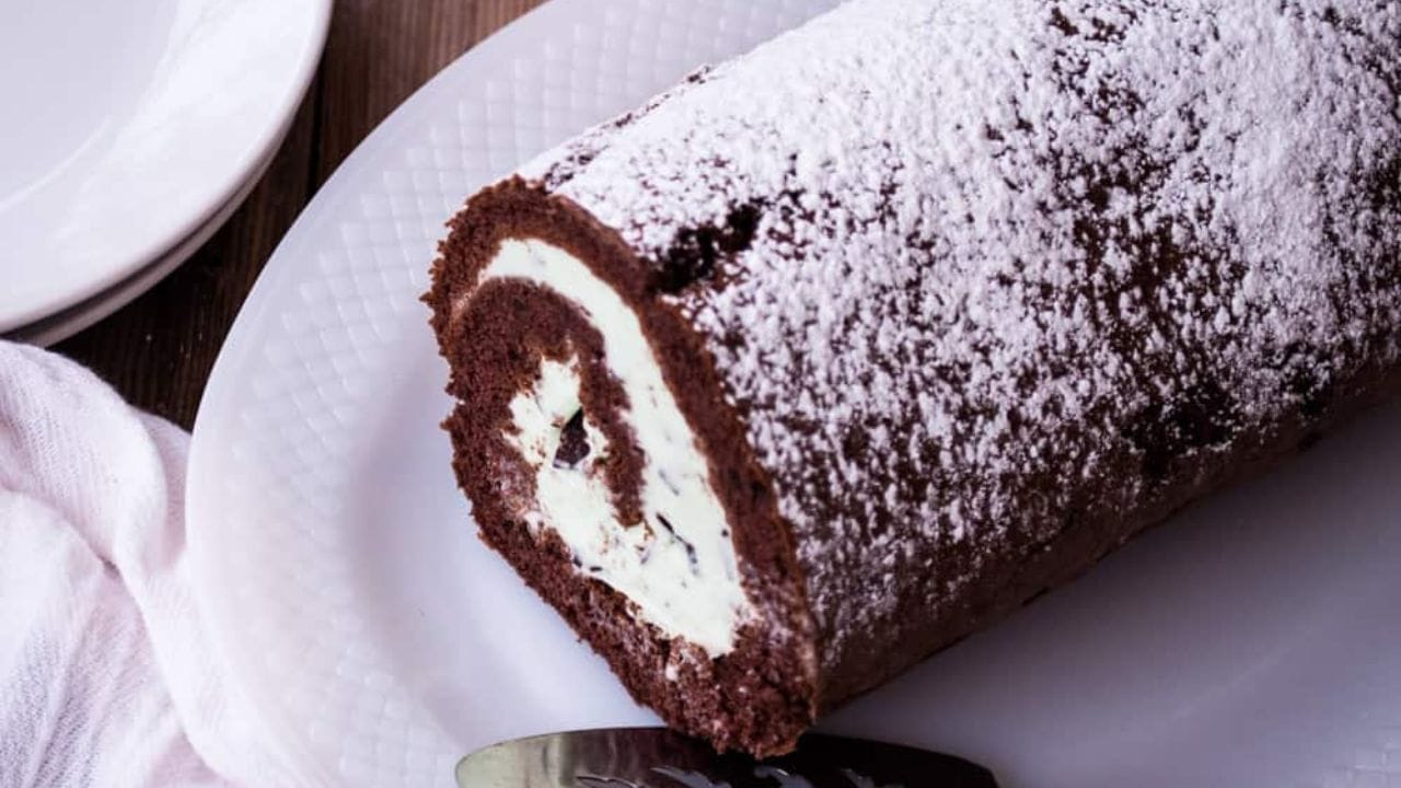Chocolate mint ice cream cake roll dusted with powdered sugar in a white plate.