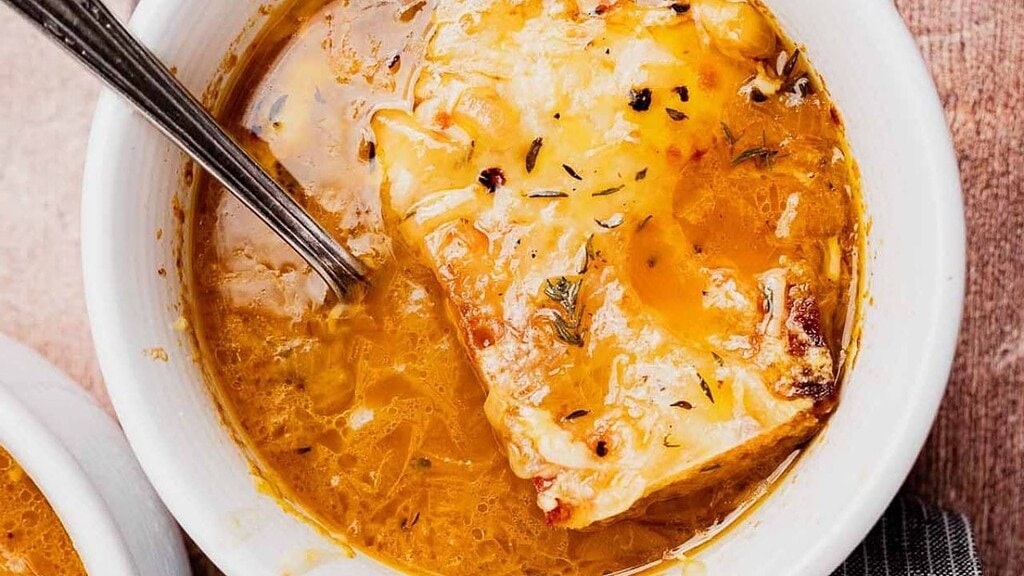 A bowl of French onion soup topped with melted cheese and herbs, with a spoon resting inside.