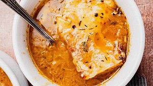 A bowl of French onion soup topped with melted cheese and herbs, with a spoon resting inside.