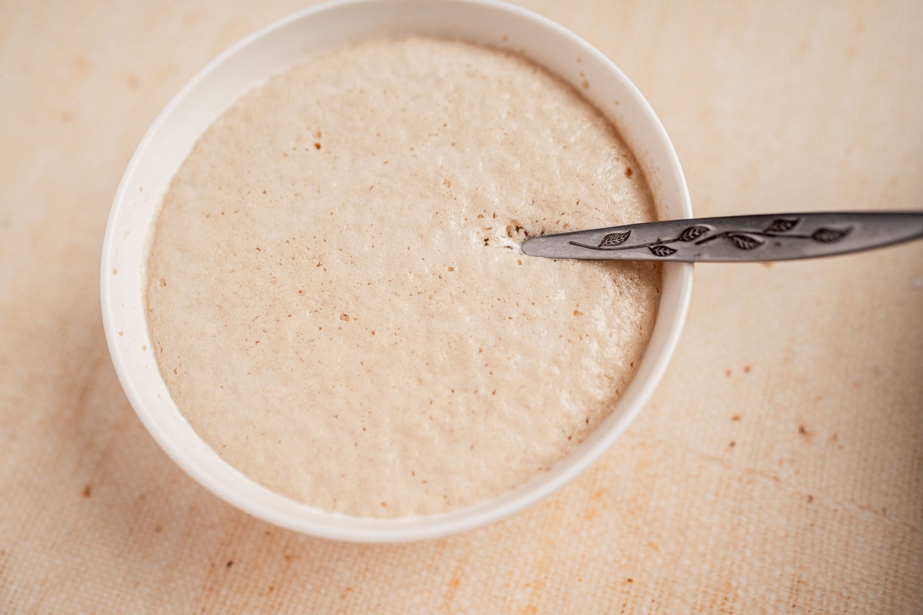 A bowl of active, bubbly sourdough starter with a spoon resting inside—perfect for creating delicious gluten free dinner rolls.