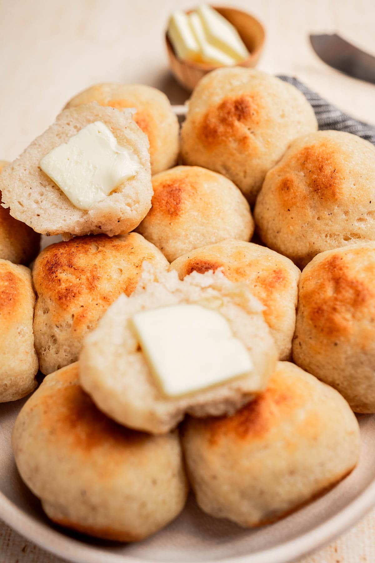 A plate of gluten free dinner rolls, some split open with slices of butter inside; a small dish with more butter is in the background.