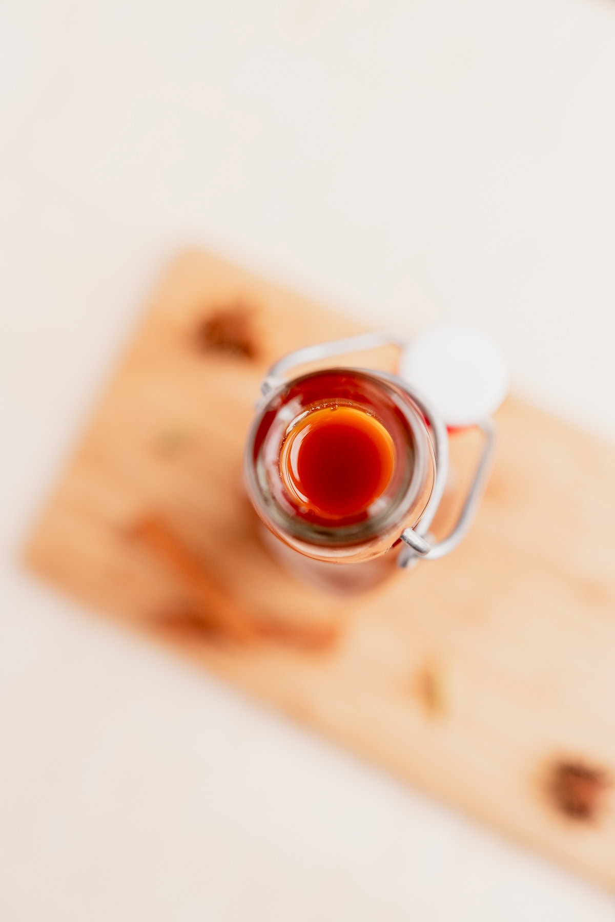 A glass jar filled with dark amber chai concentrate sits on a wooden board, photographed from above with some scattered spices around it.