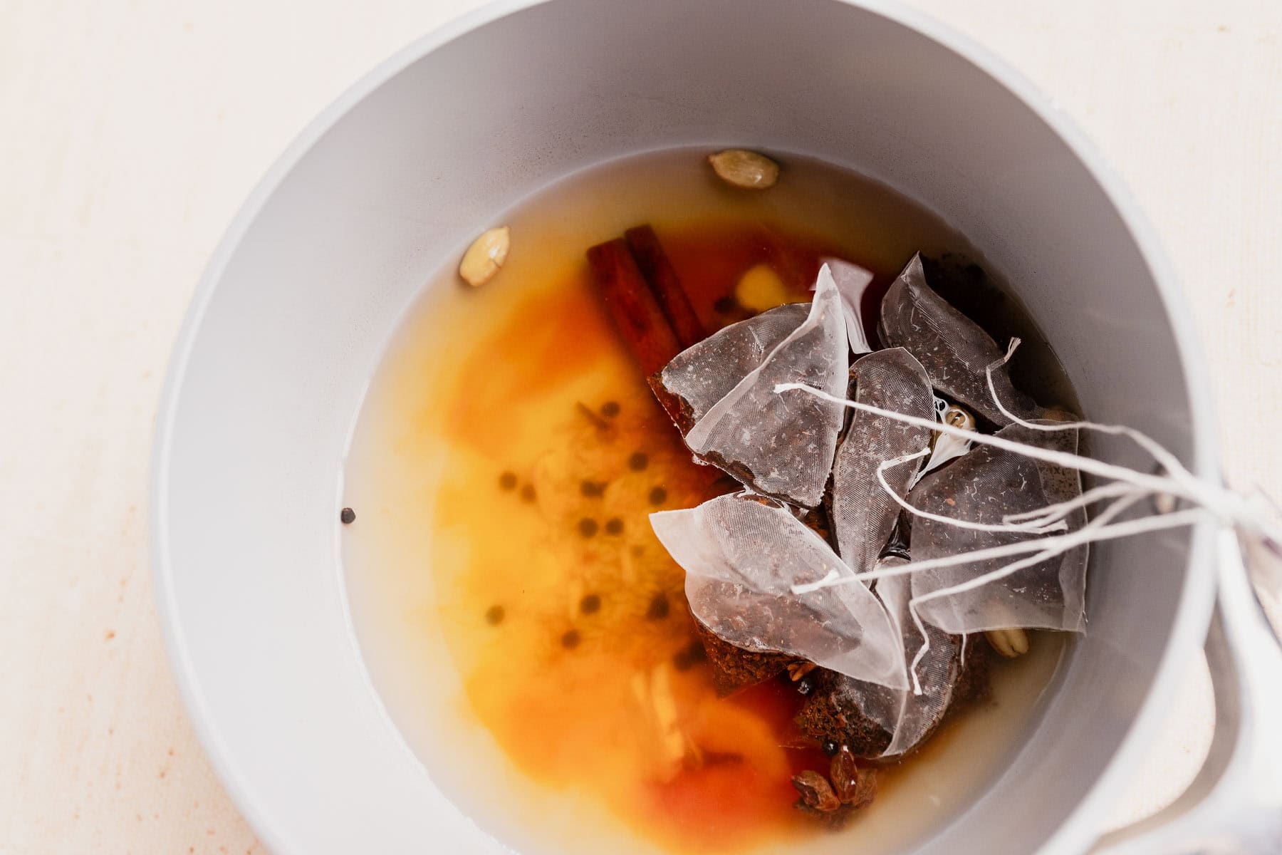 A close-up of tea bags, spices, and water in a light gray pot, with cinnamon sticks and cardamom pods visible—a perfect base for homemade chai concentrate.