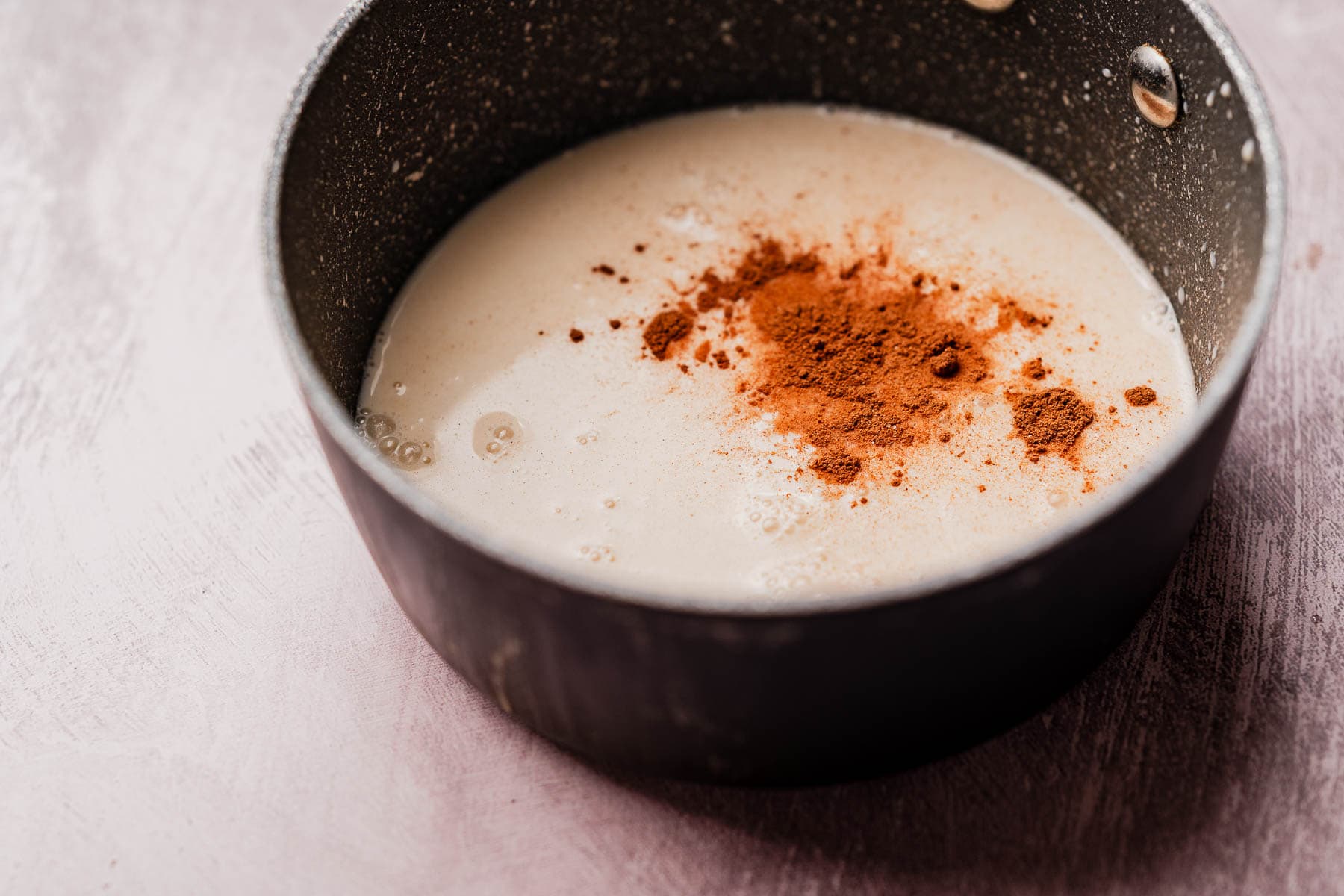 A saucepan containing a creamy liquid with a pile of ground cinnamon on top, ready to be mixed for a comforting hojicha latte.