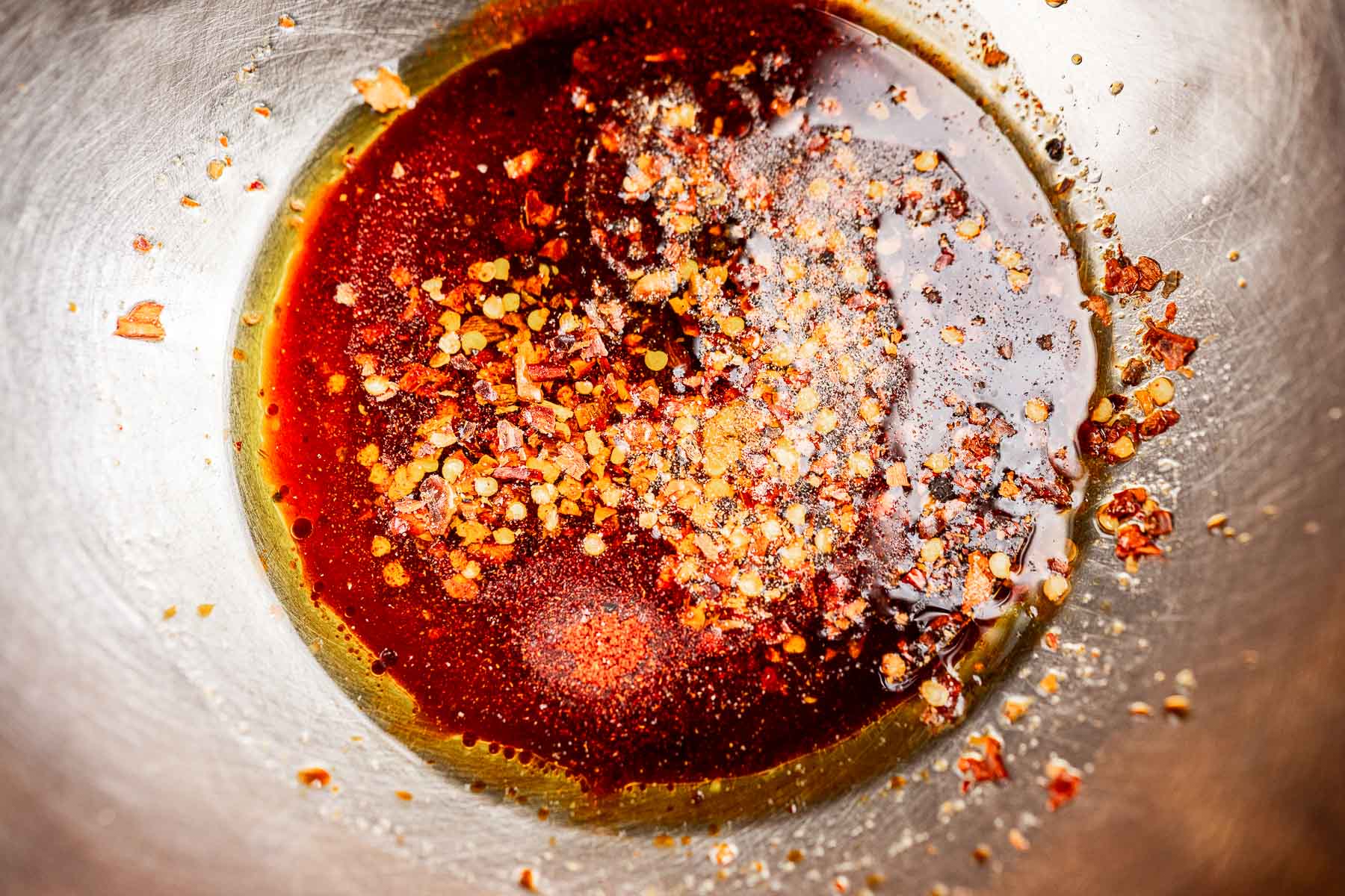 A metal bowl containing a mixture of dark liquid sauce and red pepper flakes, perfect for drizzling over roasted brussels sprouts.