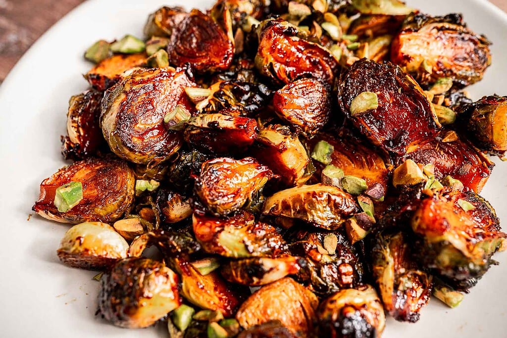 A plate of roasted Brussels sprouts garnished with chopped green herbs or vegetables, featuring crispy, browned edges that highlight the rich flavors of perfectly roasted Brussels sprouts.