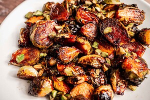 A plate of roasted Brussels sprouts garnished with chopped green herbs or vegetables, featuring crispy, browned edges that highlight the rich flavors of perfectly roasted Brussels sprouts.