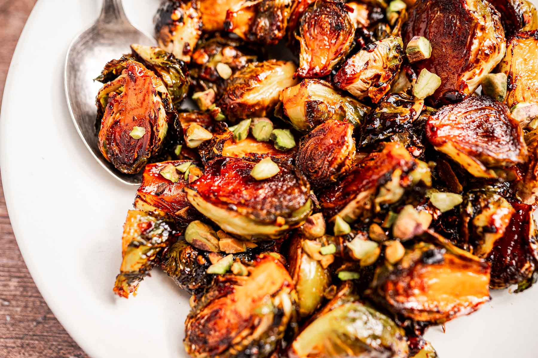 A plate of roasted Brussels sprouts garnished with chopped nuts, with a spoon visible at the edge, highlights the perfect balance of flavors and textures in this roasted Brussels sprouts dish.