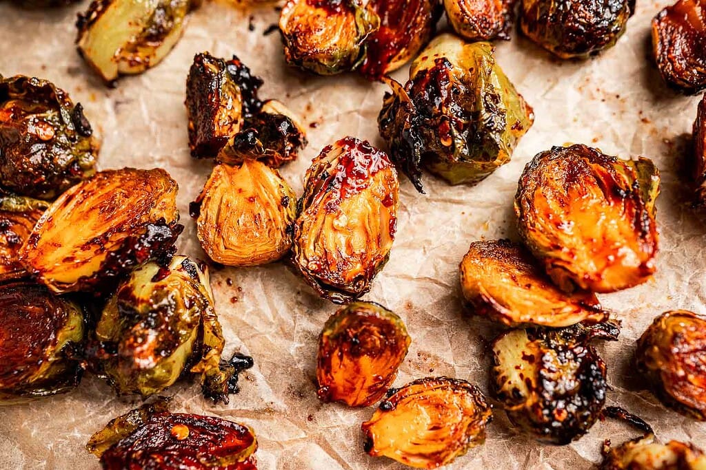 Close-up of roasted Brussels sprouts on crinkled parchment paper, highlighting the caramelized edges and charred spots that make these roasted Brussels sprouts irresistibly crispy.