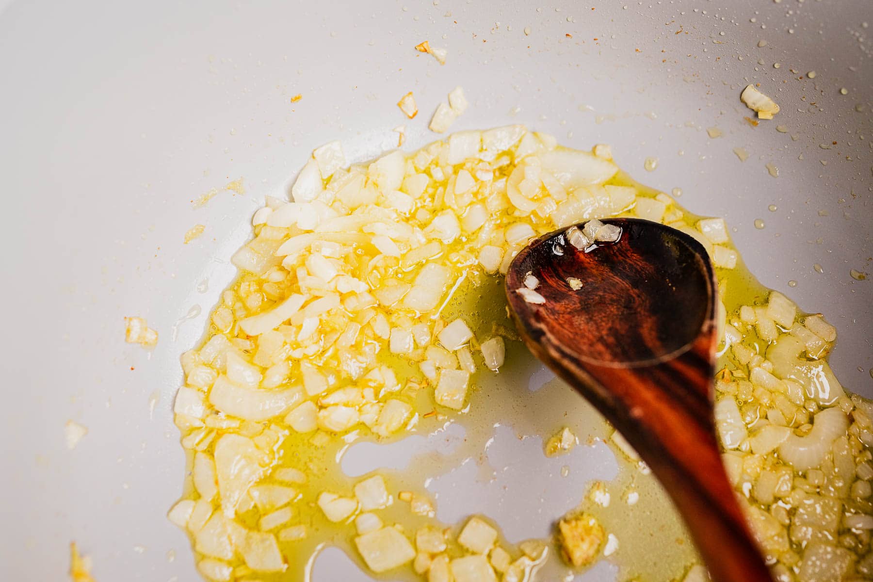 Chopped onions are sautéing in oil in a pan, being stirred with a wooden spoon as the base for a delicious pumpkin and sweet potato soup.