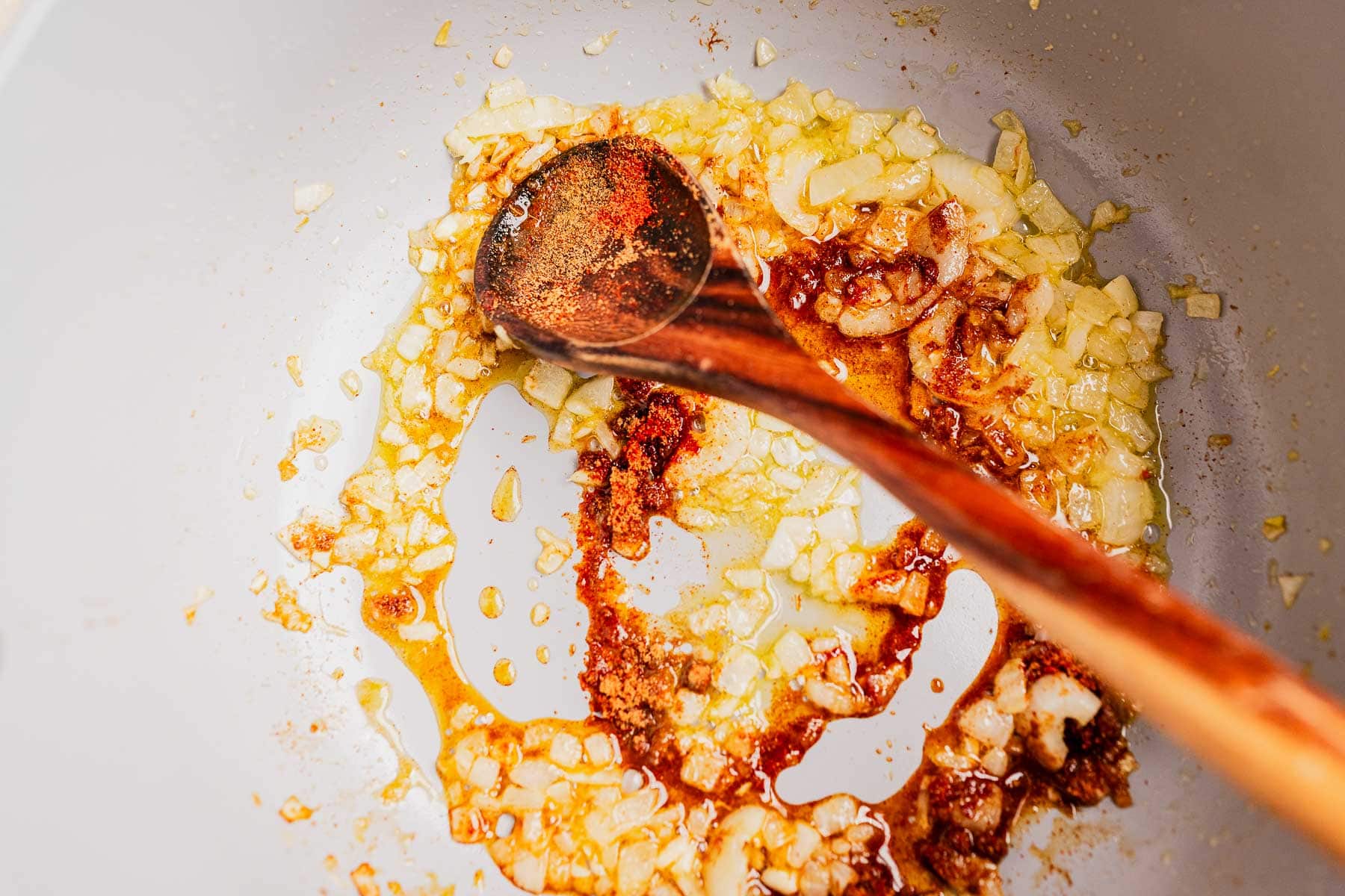 Chopped onions sautéing with oil and spices in a pan, stirred with a wooden spoon—the perfect base for a hearty pumpkin and sweet potato soup.