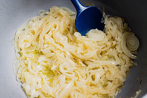 Sliced onions cooking in oil in a pan, stirred with a blue spatula—the perfect start for a delicious vegetarian French onion soup.