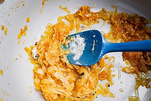 A blue spatula mixing cooked onions and powder in a white pan with some oil, the perfect base for vegetarian French onion soup.