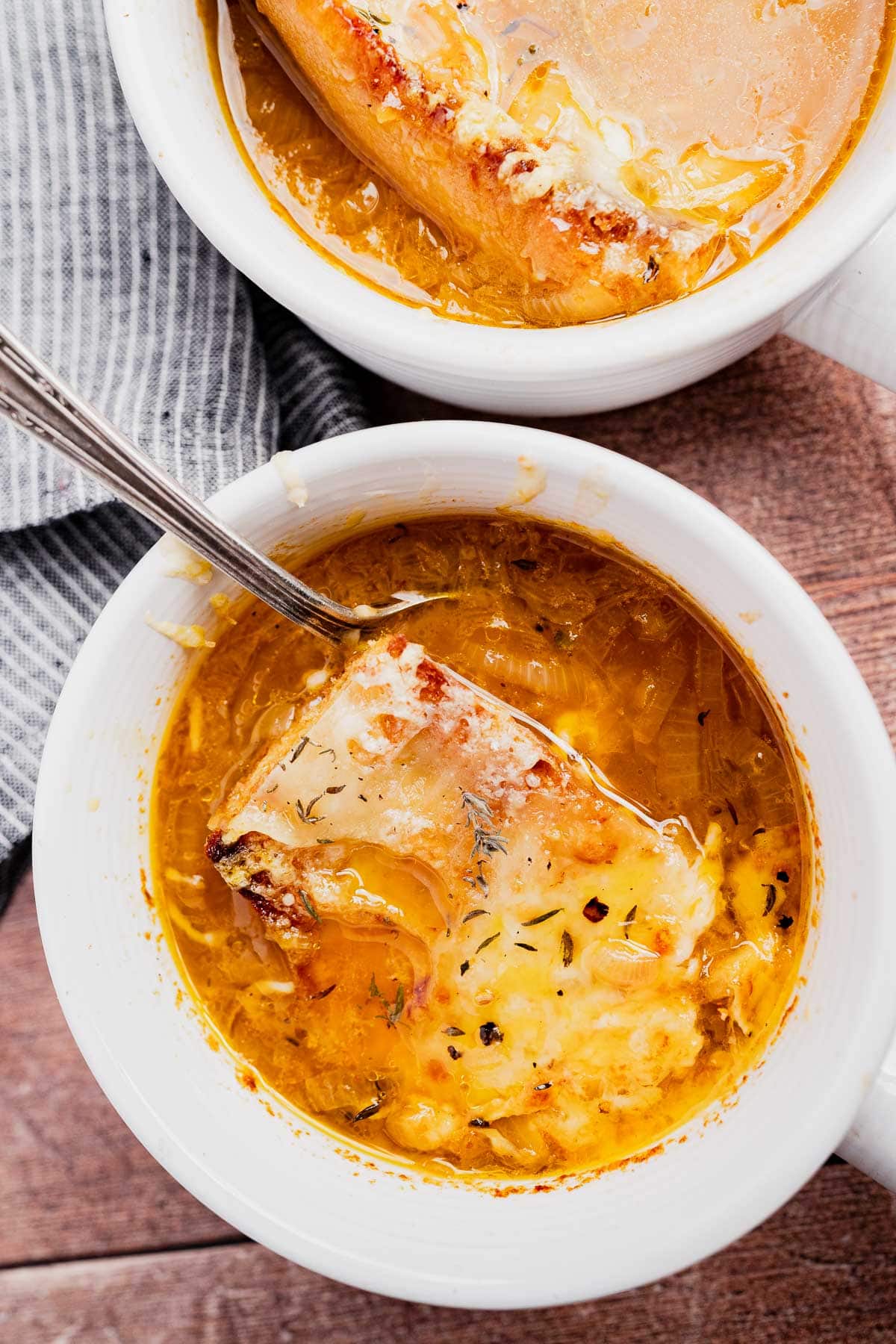 Two bowls of vegetarian French onion soup topped with melted cheese and toasted bread, one with a spoon resting inside.