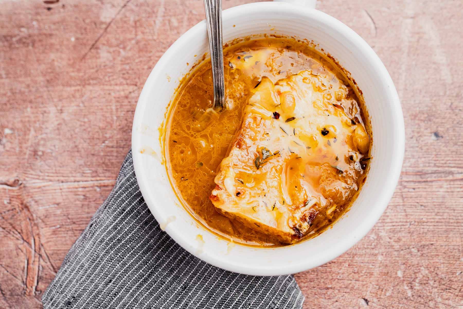 A bowl of vegetarian French onion soup topped with melted cheese and bread, with a spoon inside, placed on a gray cloth napkin.