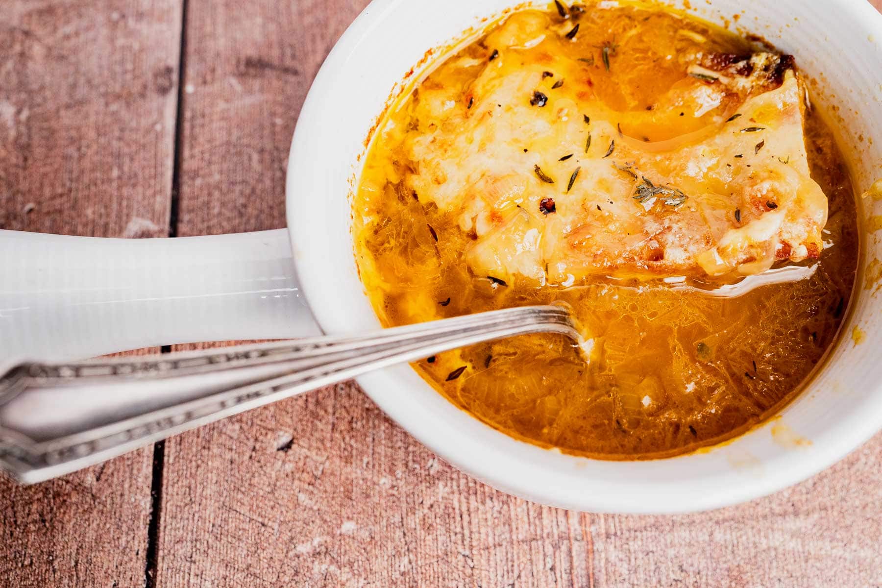 A bowl of vegetarian French onion soup topped with melted cheese and herbs, with a spoon resting inside, on a wooden surface.