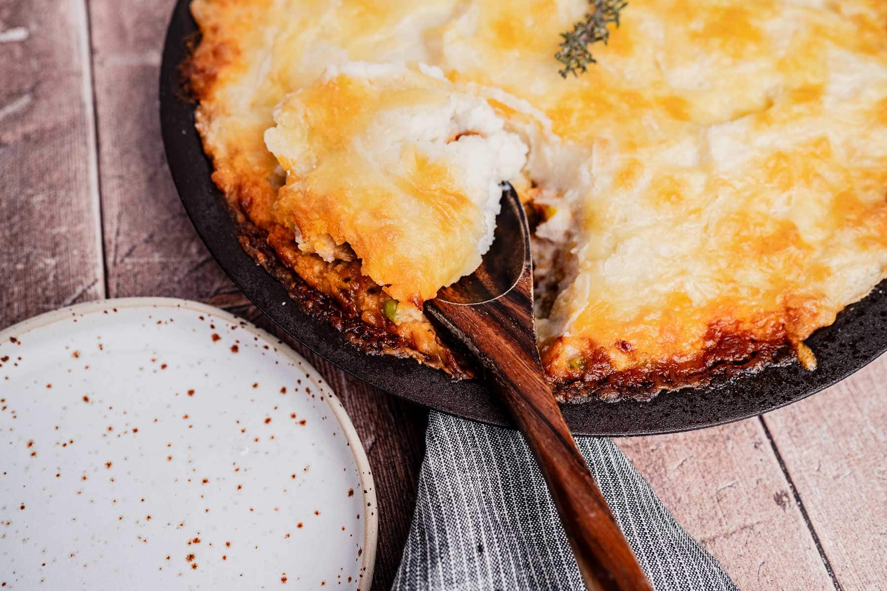A vegetarian shepherd's pie with a golden-brown mashed potato topping is being served onto a plate with a wooden spoon.
