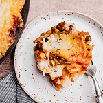 A serving of vegetarian shepherd's pie with mashed potato topping is plated beside the main dish; a sprig of thyme garnishes the food.