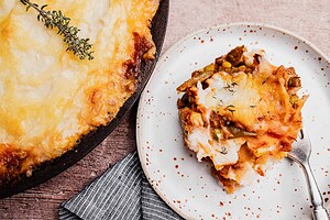 A serving of vegetarian shepherd's pie with mashed potato topping is plated beside the main dish; a sprig of thyme garnishes the food.