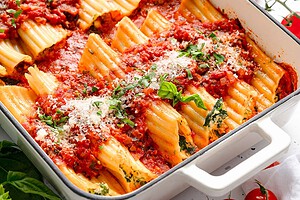 Baked manicotti pasta filled with ricotta and spinach, topped with tomato sauce, grated cheese, and fresh basil in a white casserole dish.