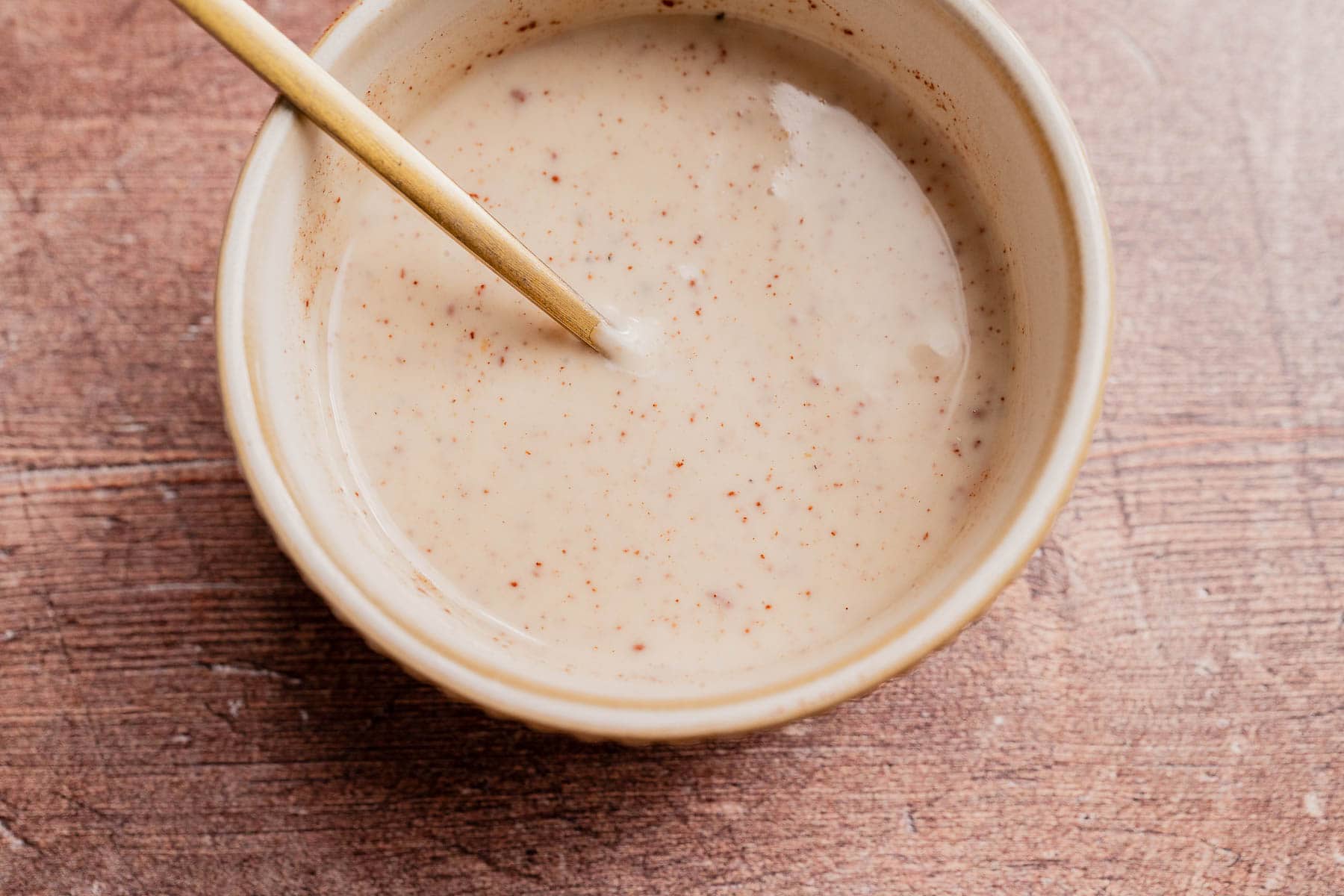 A ceramic bowl filled with a creamy, speckled sauce or dressing for a Thanksgiving fruit salad, with a spoon resting inside, placed on a wooden surface.