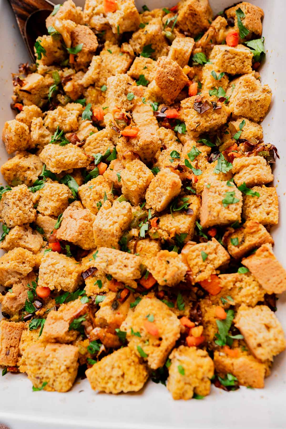 A close-up of a baking dish filled with gluten free cornbread stuffing, garnished with chopped vegetables and fresh herbs.