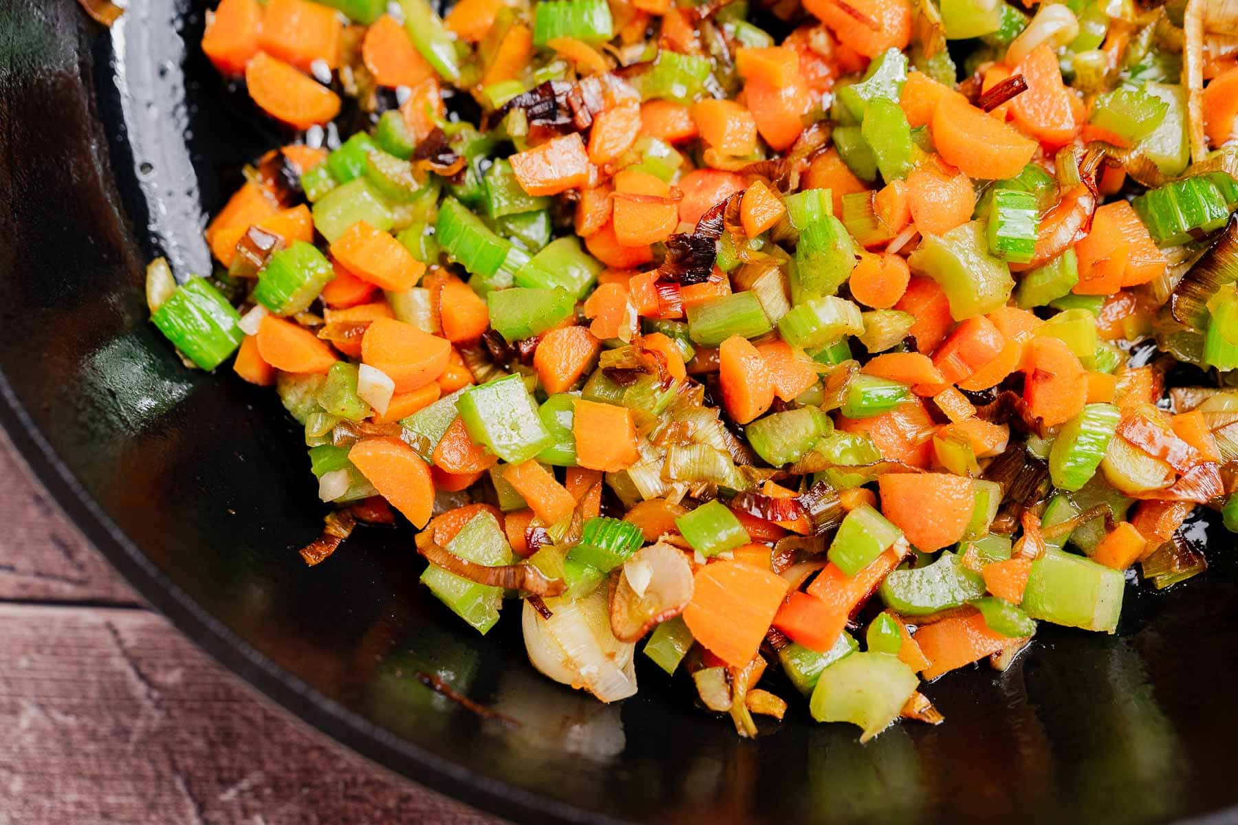 Diced carrots, celery, and onions are sautéing in a black skillet as the savory base for a delicious gluten free cornbread stuffing.