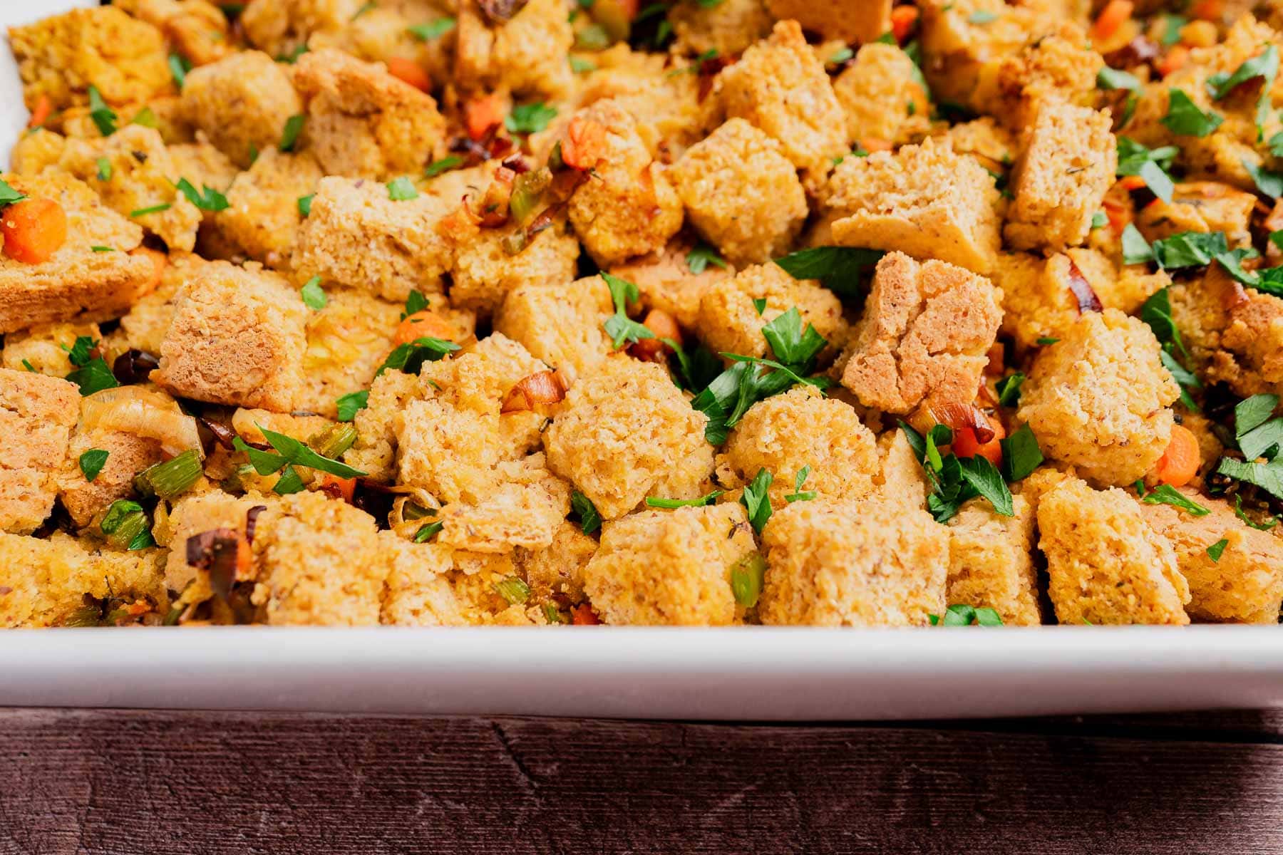 Close-up of a dish filled with gluten free cornbread stuffing, mixed with chopped vegetables and garnished with fresh herbs.