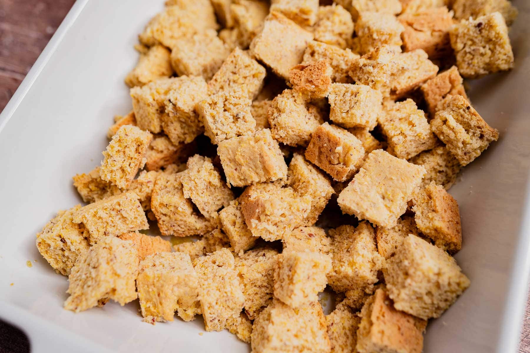 Close-up of a white dish filled with cubed gluten free cornbread stuffing pieces.