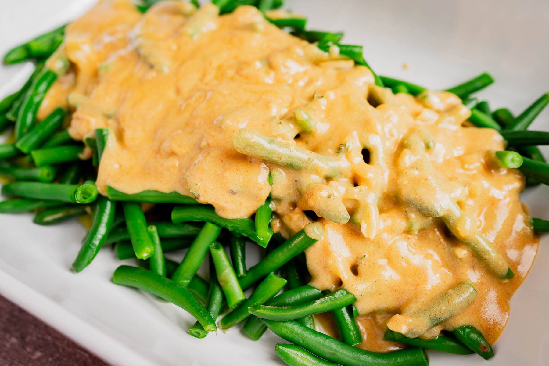 Gluten free vegan green bean casserole features green beans topped with a creamy brown sauce, beautifully arranged on a white plate.