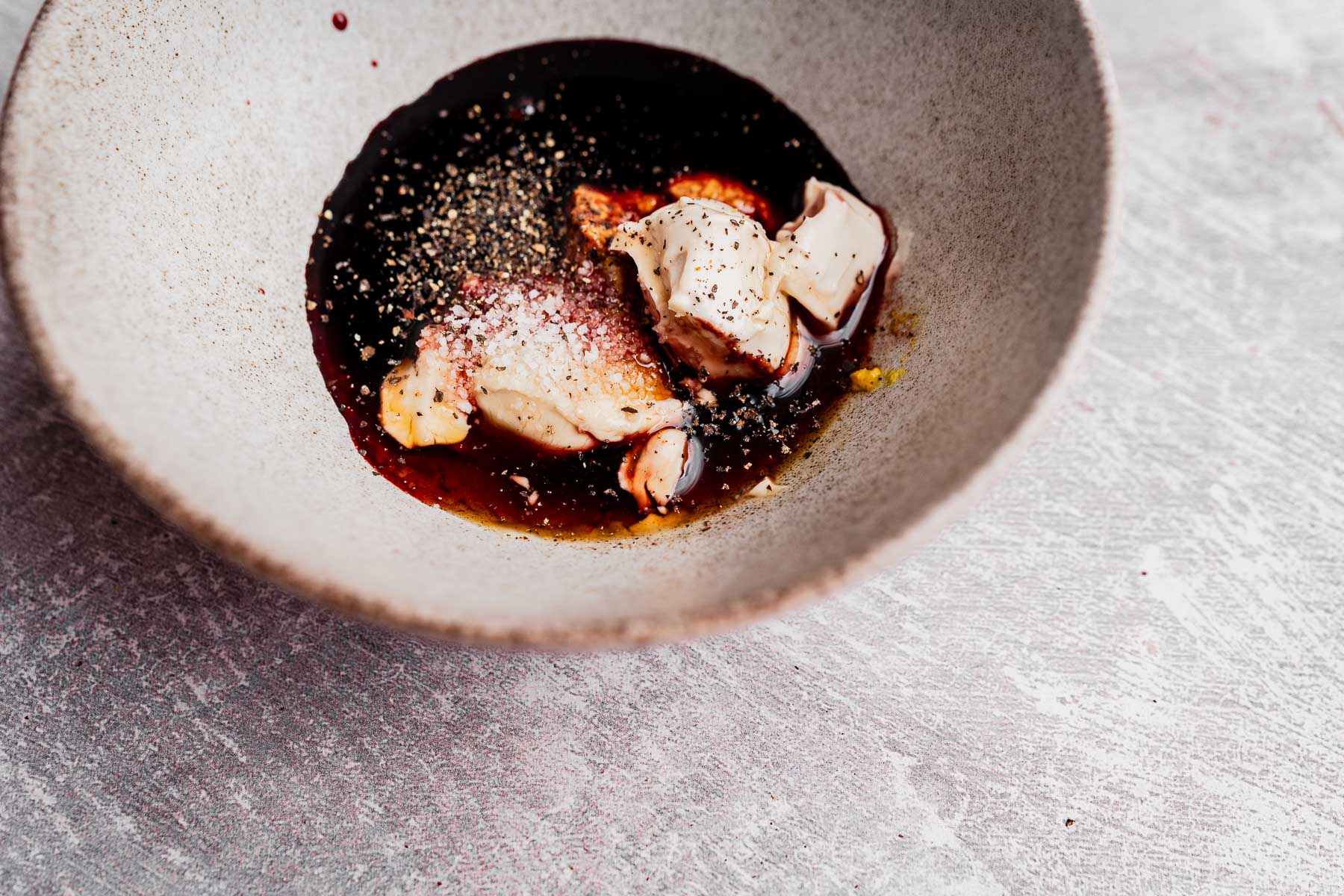 A bowl containing soy sauce, mayonnaise, pepper, Pomegranate Salad Dressing, and other seasonings on a light textured surface.