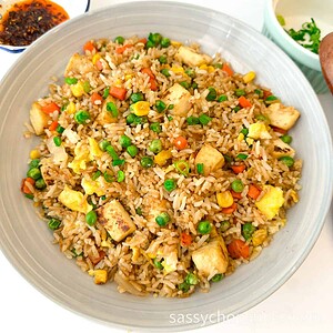 A plate of vegetable fried rice with tofu, green peas, corn, carrots, and scrambled egg, served on a light-colored dish.