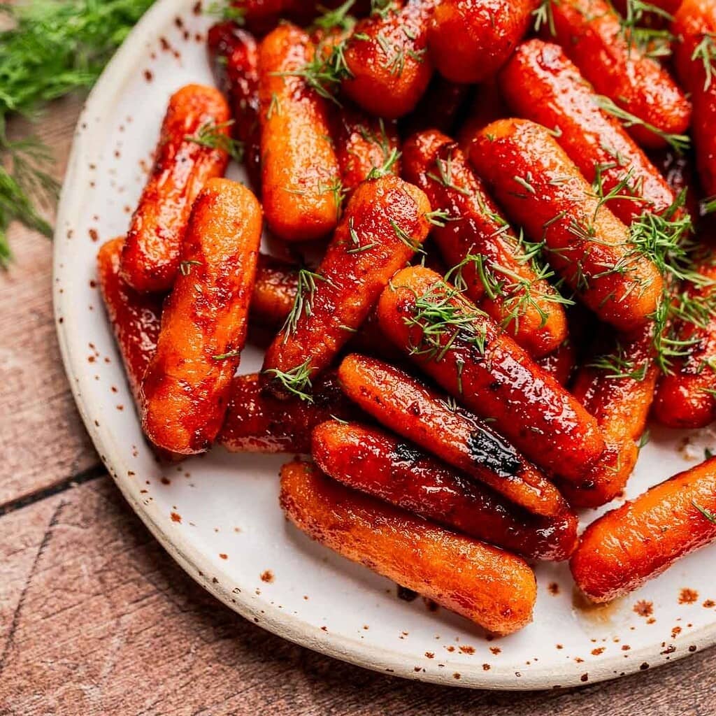 Brown sugar glazed carrots roasted to perfection, garnished with fresh dill and served on a white plate.