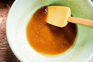 A mixing bowl containing a brown liquid mixture—perfect for making brown sugar glazed carrots—with a yellow spatula resting inside.