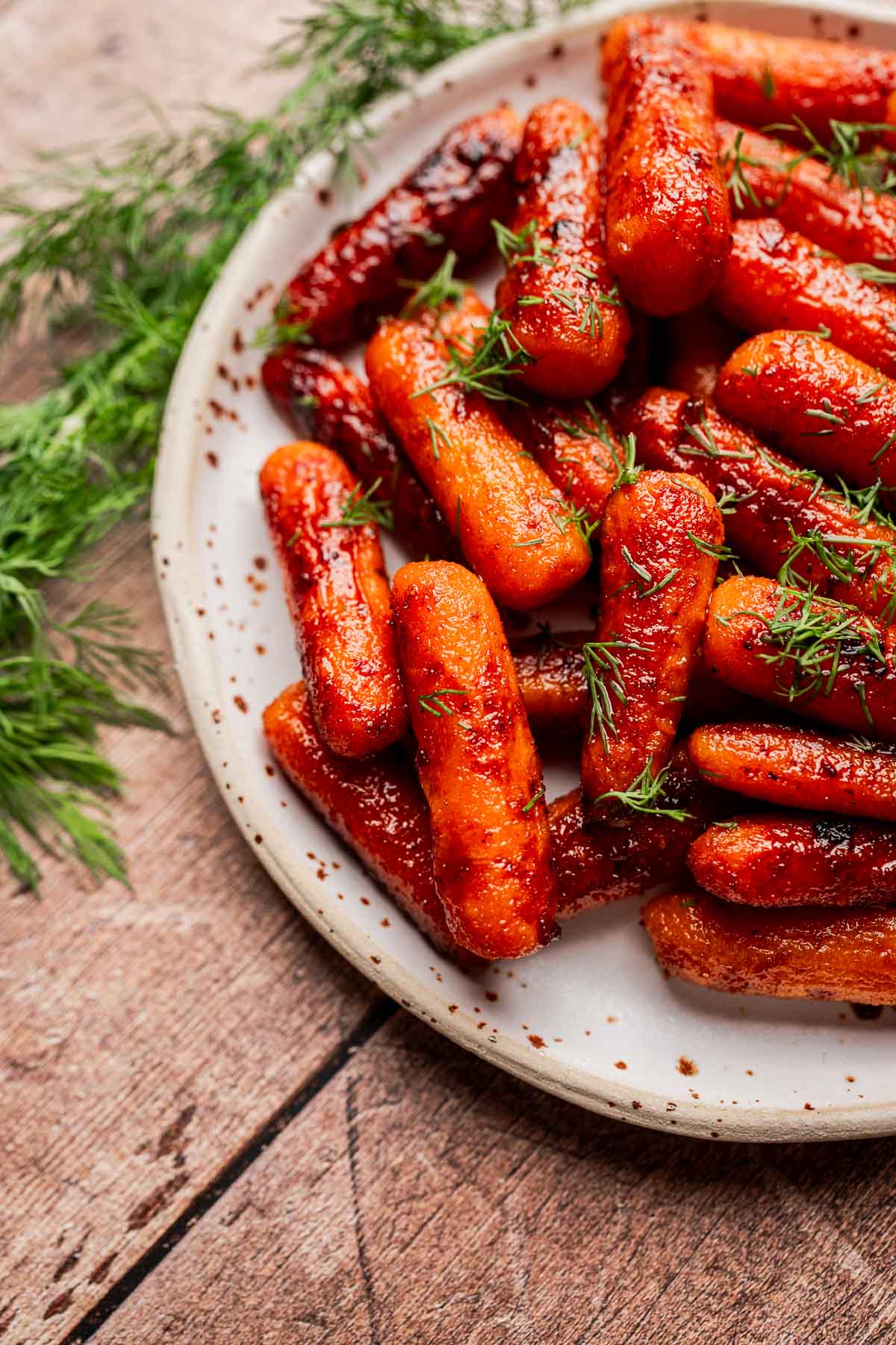 A plate of brown sugar glazed carrots garnished with fresh dill, placed on a wooden table.