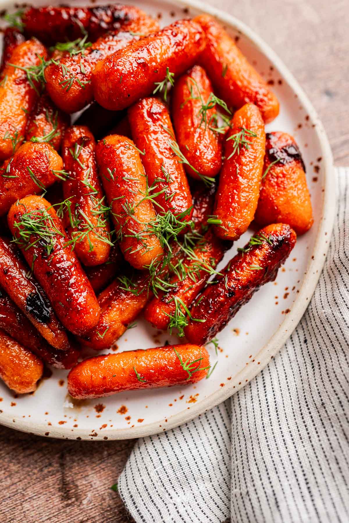 A plate of brown sugar glazed carrots garnished with fresh herbs, placed on a striped cloth napkin.
