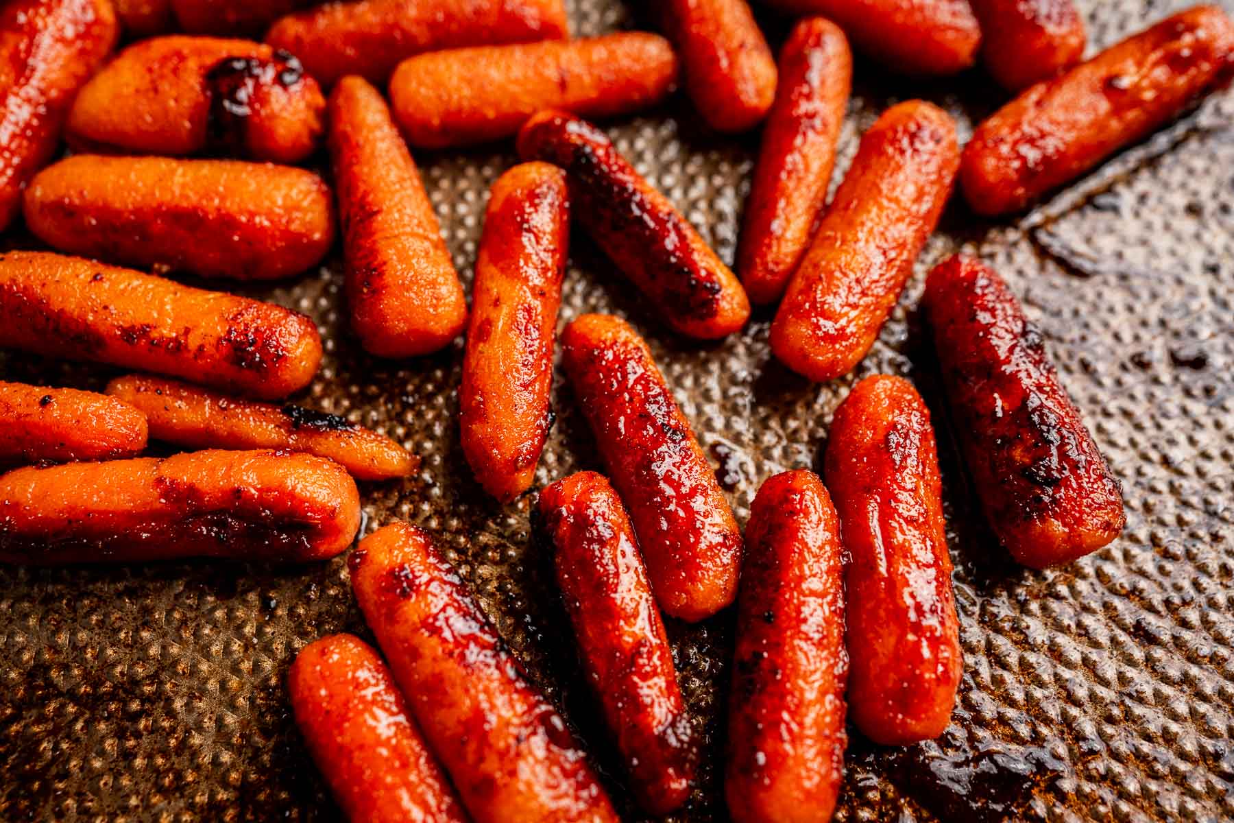 Close-up of brown sugar glazed carrots, their caramelized glaze glistening atop a textured baking sheet.