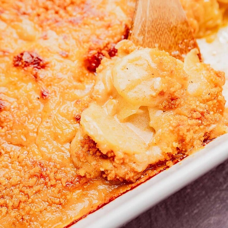 Close-up of a serving of cheesy potato casserole gratin being scooped from a baking dish with a wooden spoon.